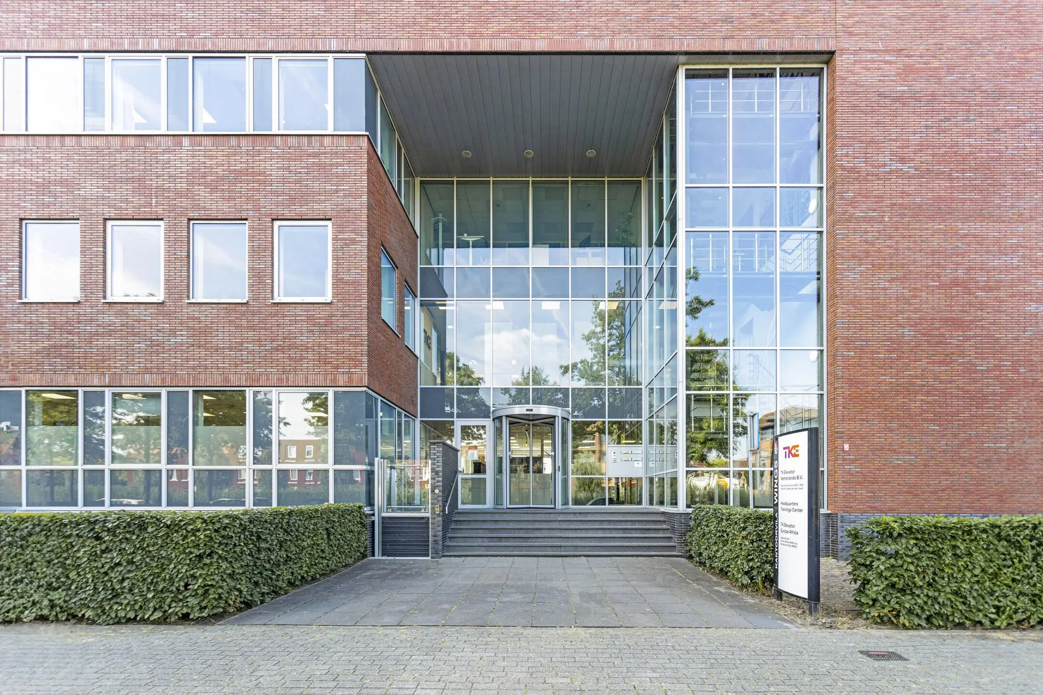 De hoofdingang van een modern kantoorgebouw aan de Fascinatio Boulevard met veel glas en een bakstenen gevel.
